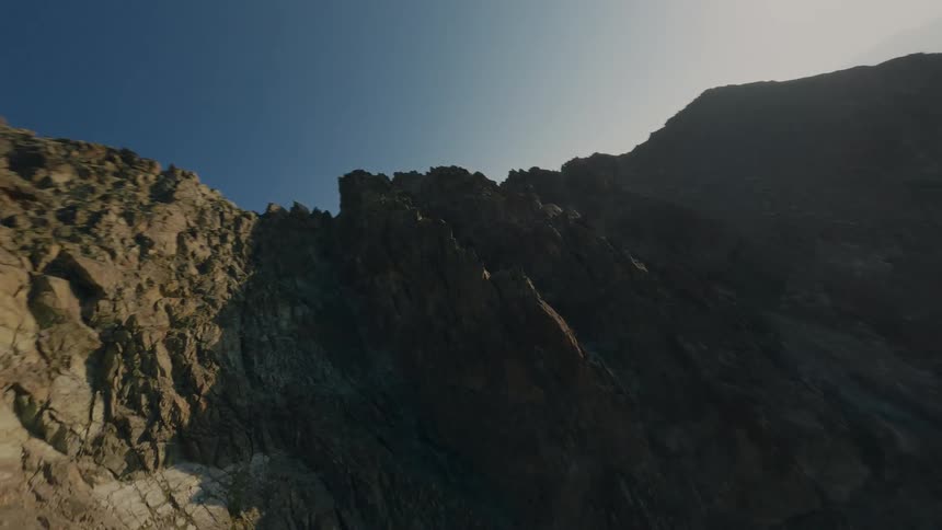 Thrilling first-person view drone flight dives down the side of a rugged, rocky mountain peak under a clear sky
