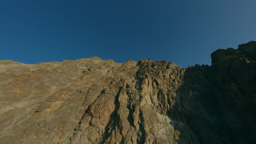 A thrilling FPV drone dives down the steep and rugged face of a mountain peak