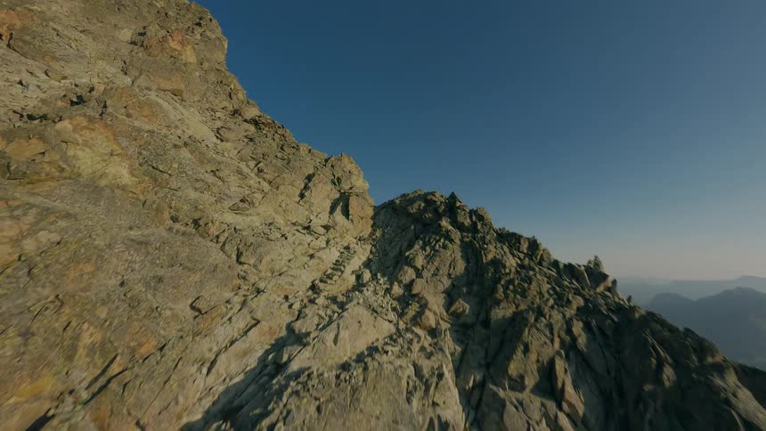 A dynamic FPV drone shot soars up a rugged mountain face, passing by climbers on their way to the summit and revealing the vast mountain landscape beyond