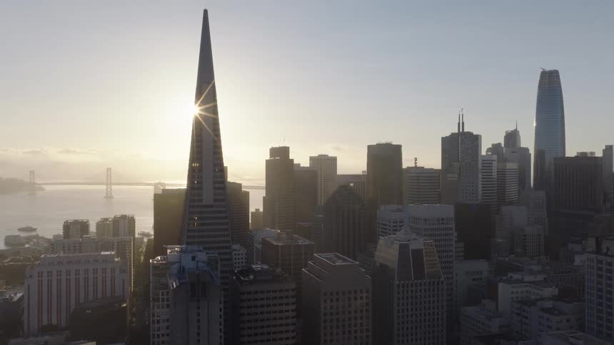 A stunning aerial view of the San Francisco skyline, with the sun rising and creating a brilliant sunburst behind the iconic Transamerica Pyramid