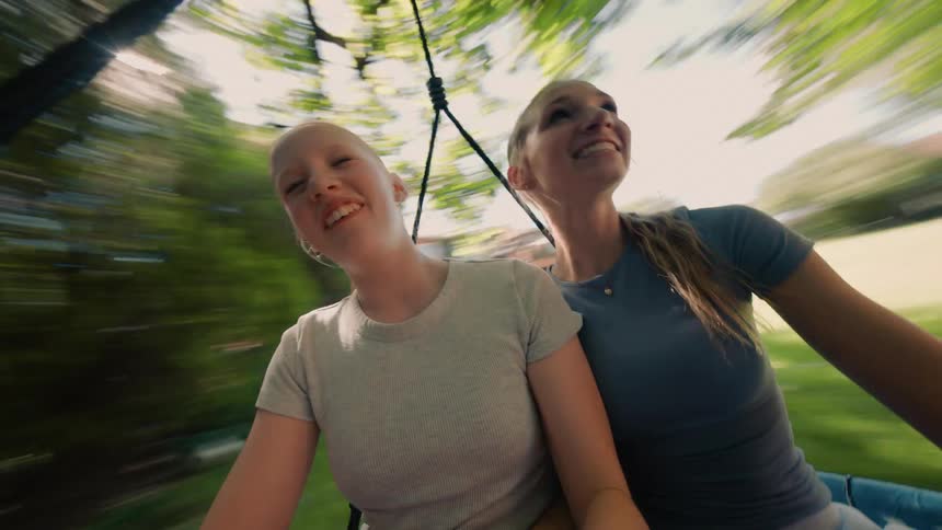 A POV shot of two joyful teenage girls laughing and smiling while spinning rapidly on a swing in a backyard