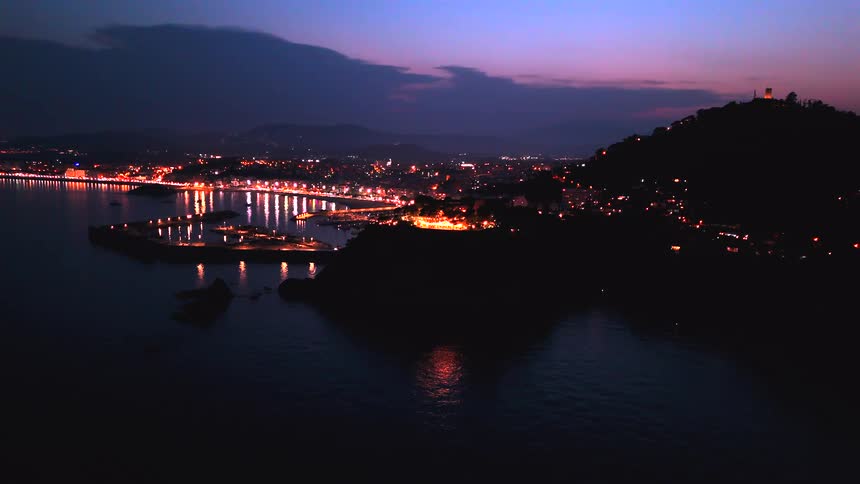 Scenic wide shot of a glowing seaside city and its harbor during a vibrant twilight