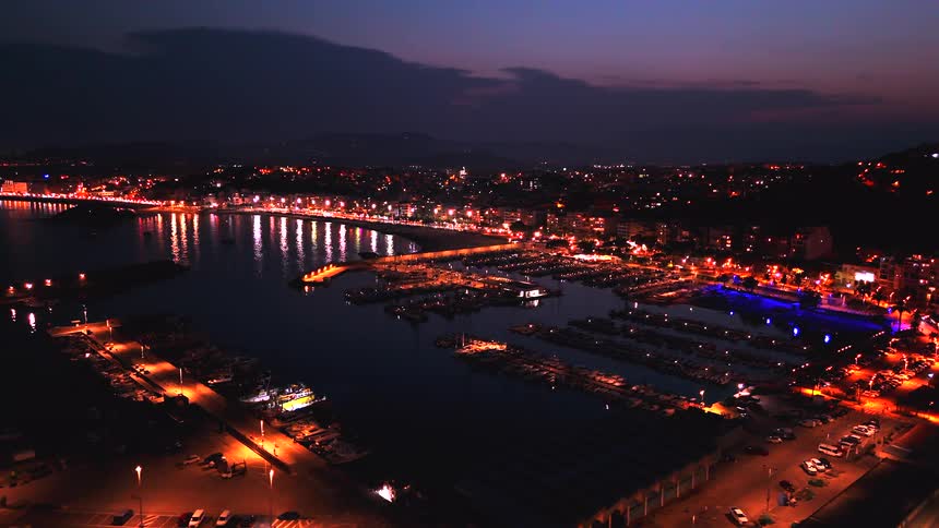 An awe-inspiring aerial view of a bustling coastal town and its vibrant marina, beautifully illuminated at dusk
