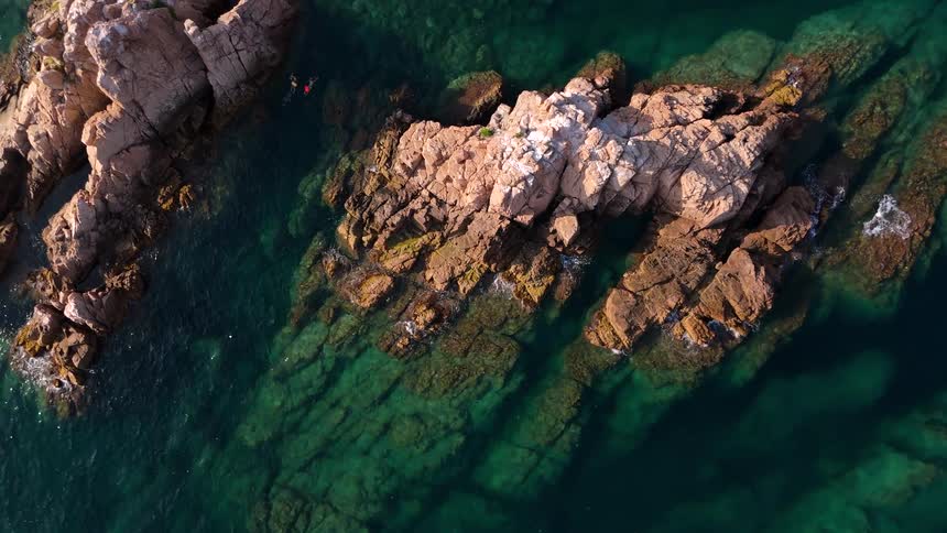 Top-down drone footage slowly pans over a beautiful rocky islet in calm, clear turquoise waters