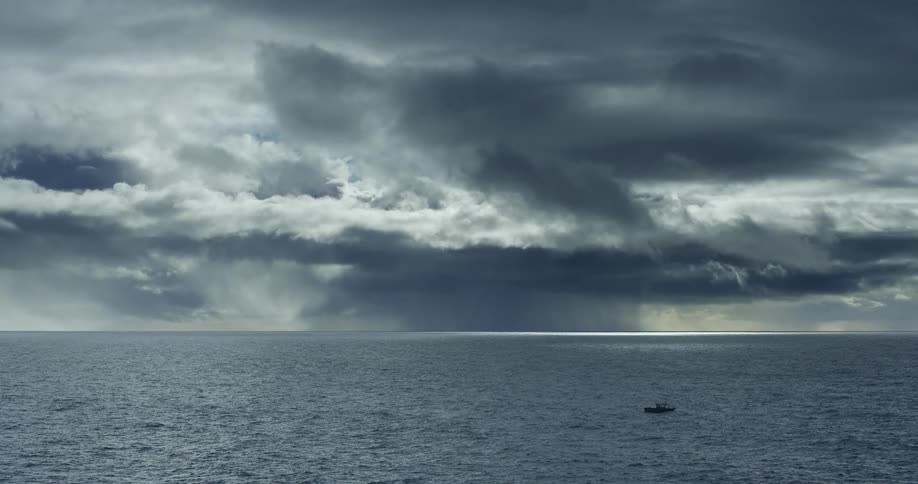Dramatic storm clouds gather over a vast, open ocean where a lone fishing boat sits under a distant downpour