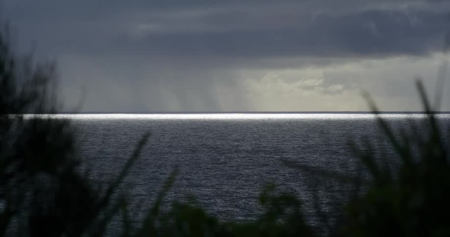 A dramatic view of a rain squall over the dark ocean with a silver line of light on the horizon