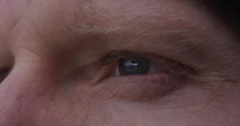 An extreme close-up of a human eye blinking slowly, revealing detailed textures and reflections