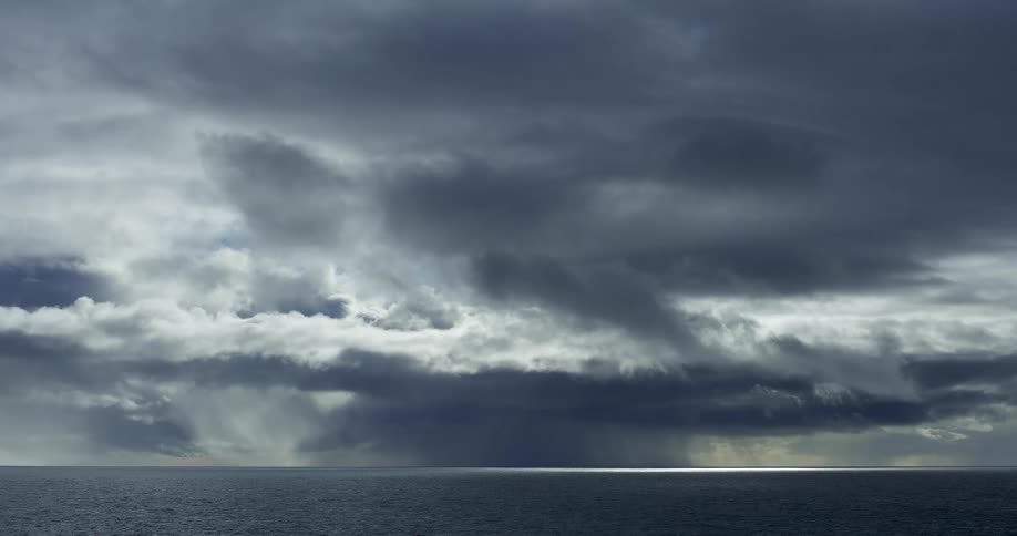 A dramatic cinemagraph shows ominous storm clouds releasing rain over the ocean as sunlight breaks through