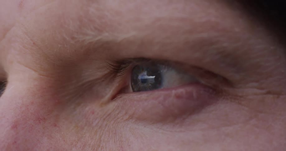 A macro shot of a human blue eye slowly opening as a tear begins to well up in the corner