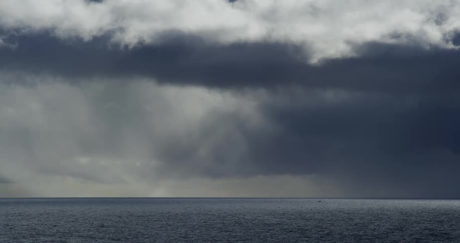 Ominous storm clouds hover over the dark ocean, with rain falling in the distance