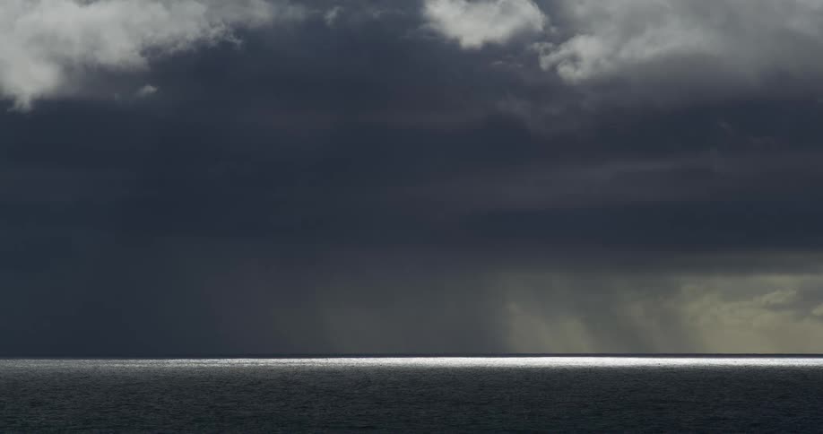 A powerful storm front with dark, ominous clouds unleashes rain over the open ocean, while a sliver of light illuminates the horizon