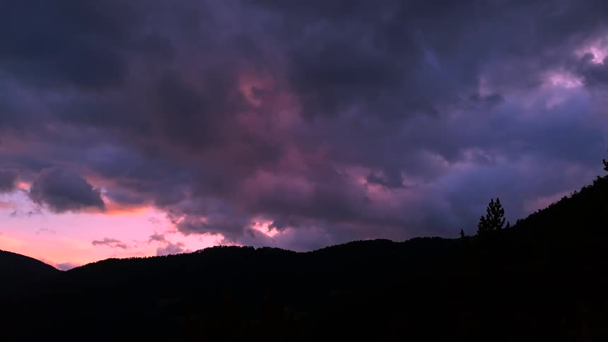 Vibrant pink and purple clouds drift across the sky during a dramatic sunset over silhouetted mountains