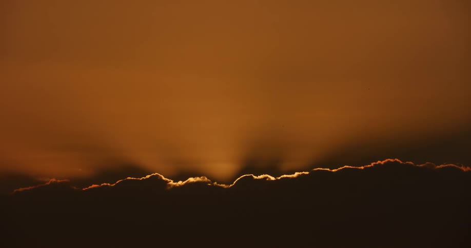 Golden sunbeams radiate from behind a dark silhouetted cloud during a stunning sunset