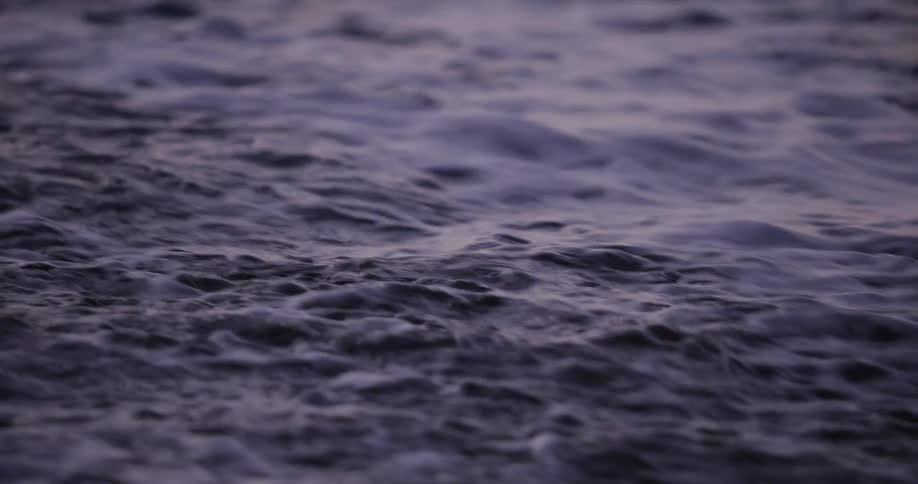 A mesmerizing close-up of foamy, purple-hued ocean water receding in slow motion at twilight