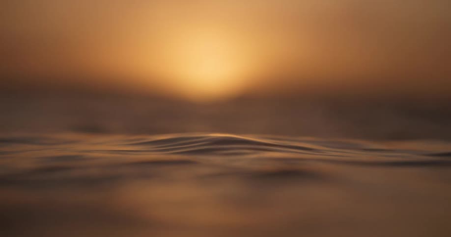 A serene close-up of gentle water ripples glowing in the warm, golden light of a dreamy sunset