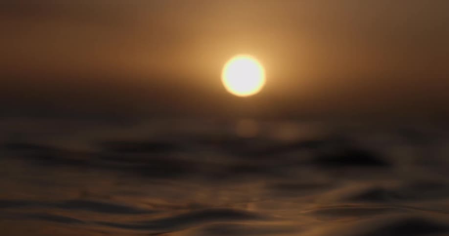 Dreamy slow motion footage captures the golden sun rising over the calm, undulating surface of the ocean