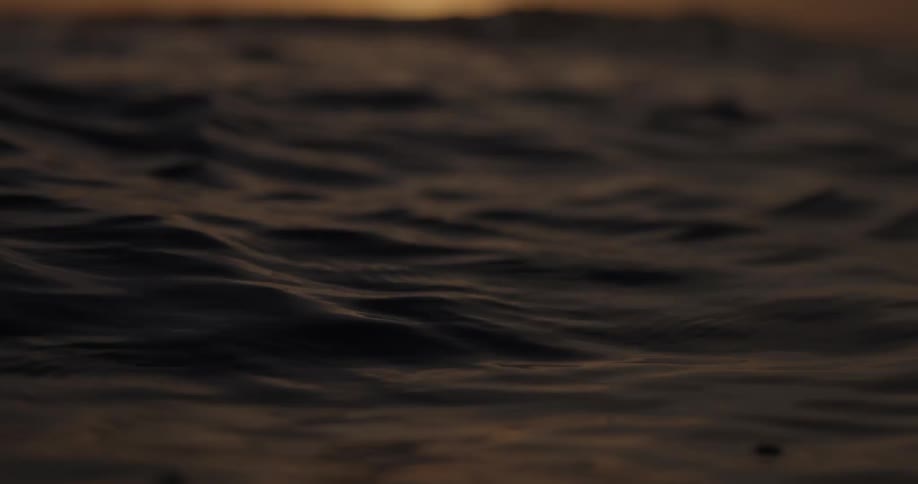 Calm ocean waves ripple in slow motion as the focus reveals a stunning golden sunrise on the horizon