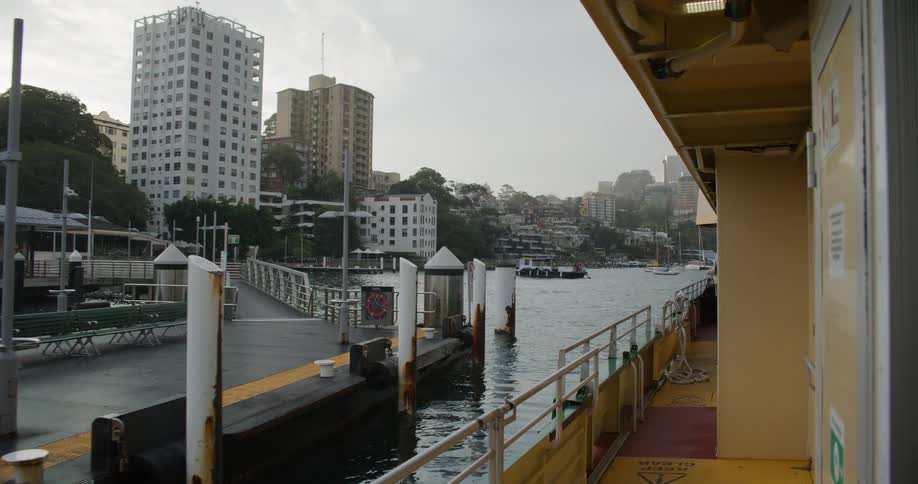 A view from a ferry as it slowly departs from the McMahons Point wharf, revealing the Sydney city harbor and shoreline