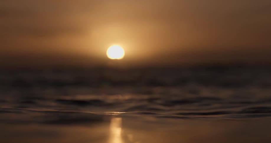 A serene slow-motion close-up of dark ocean waves rolling peacefully as the golden sun sets on the horizon