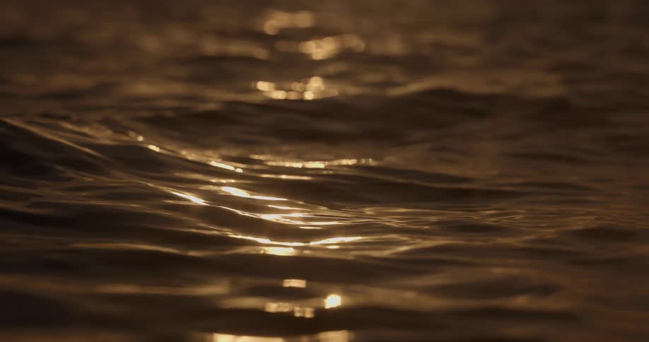 Golden hour light reflects and sparkles on the surface of gently moving water in slow motion
