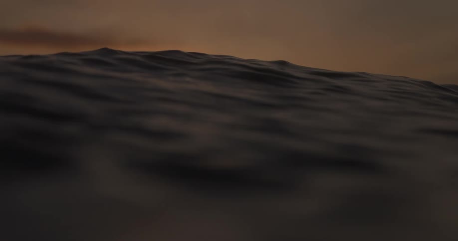 A serene close-up of gentle ocean waves at water level as the golden sun dips below the horizon