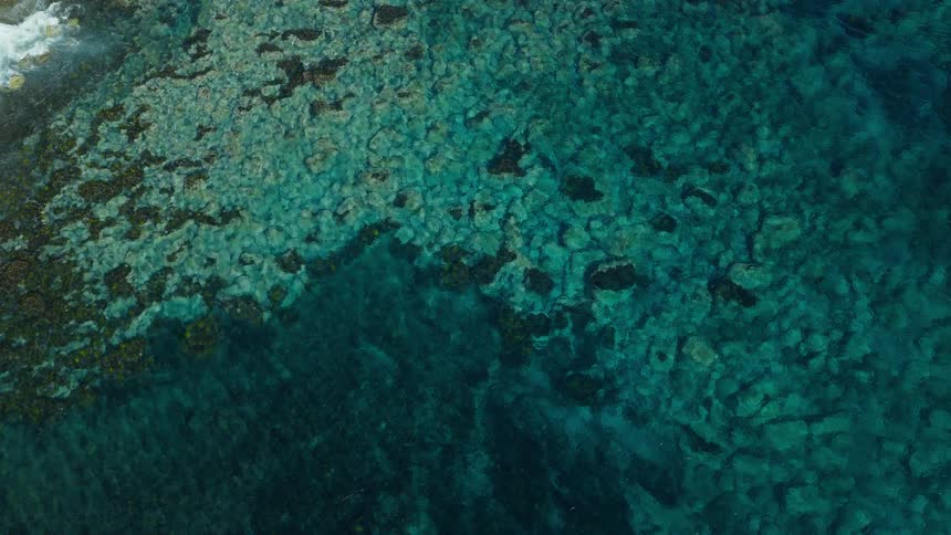 An abstract top-down aerial view of serene turquoise ocean water gently rippling over a shallow, rocky reef