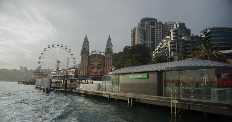 A scenic view from the water of Sydney's iconic Luna Park and the Milsons Point ferry wharf under an overcast sky