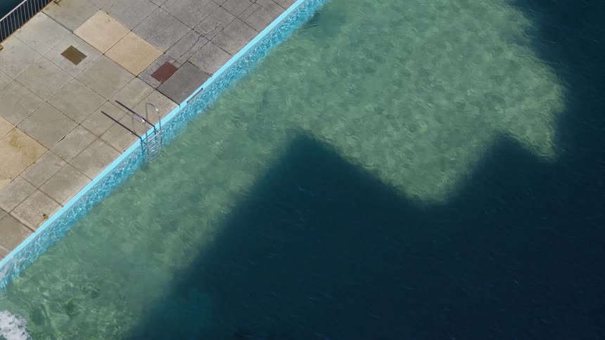 A tranquil top-down view of a sunlit swimming pool with a distinct shadow cast across its clear turquoise water