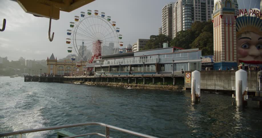 A ferry pulls away from the pier at Luna Park in Sydney, revealing the iconic face entrance and colorful Ferris wheel
