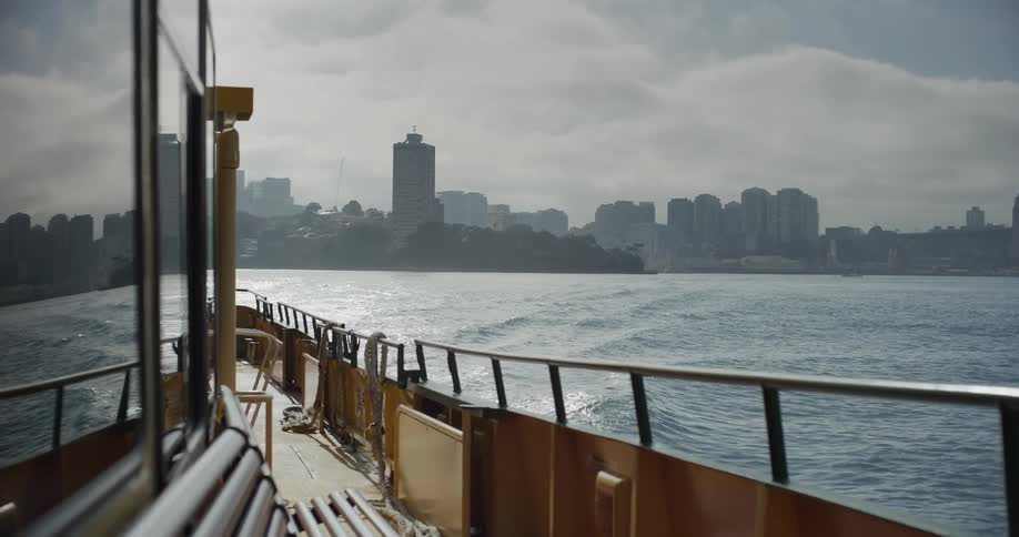 A view from the side of a moving ferry of the Sydney city skyline on an overcast day