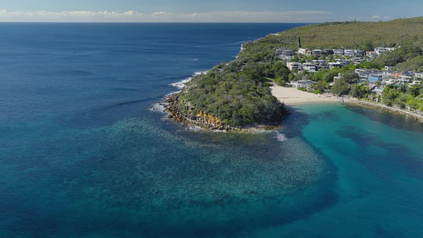 A stunning static aerial view of a picturesque coastline featuring a beautiful cove with turquoise water, a sandy beach, and a green headland