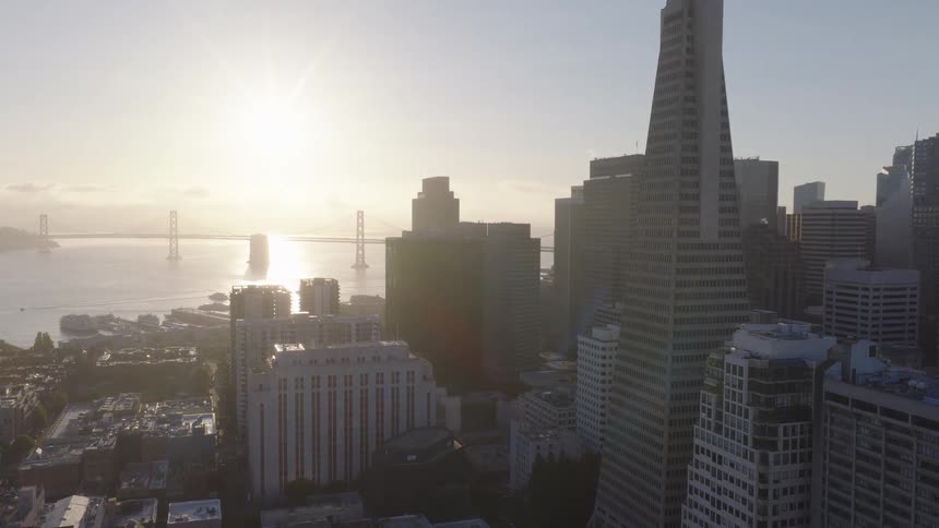 A slow aerial pullback reveals the iconic San Francisco skyline with the Transamerica Pyramid and Bay Bridge during a brilliant sunrise