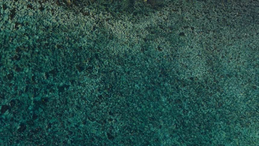 A mesmerizing top-down aerial view of clear turquoise ocean water rippling over a rocky seabed