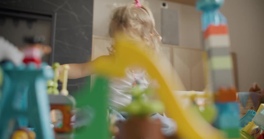 A cute blonde toddler concentrates on playing with her colorful toy playset on the floor of her room