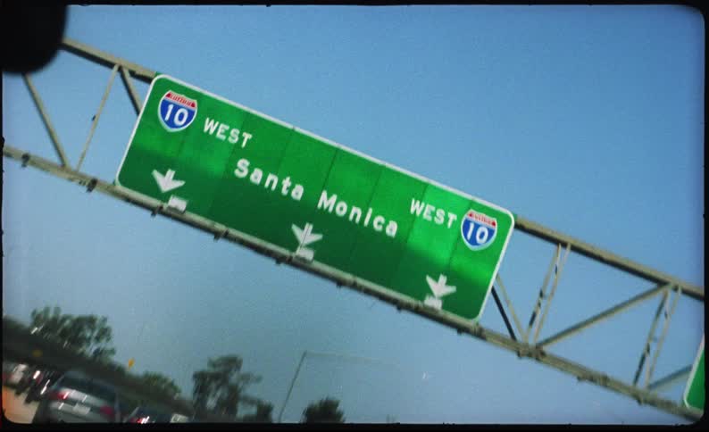 Point-of-view shot from a car driving under the Santa Monica freeway sign on the 10 West in Los Angeles on a sunny day, captured on vintage film