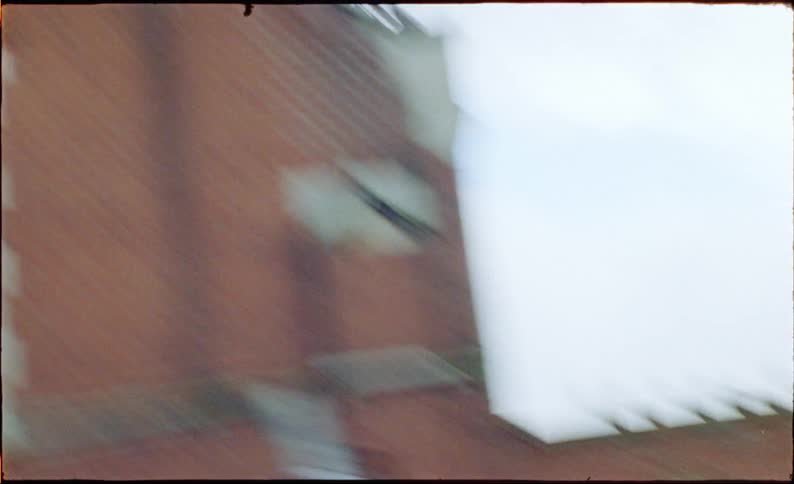 Super 8mm footage captures a flock of pigeons taking flight before a blurry, fast-paced pan across a city street