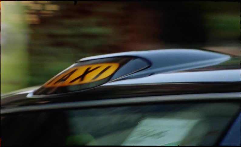 A vintage film close-up of a classic London taxi driving through the city streets