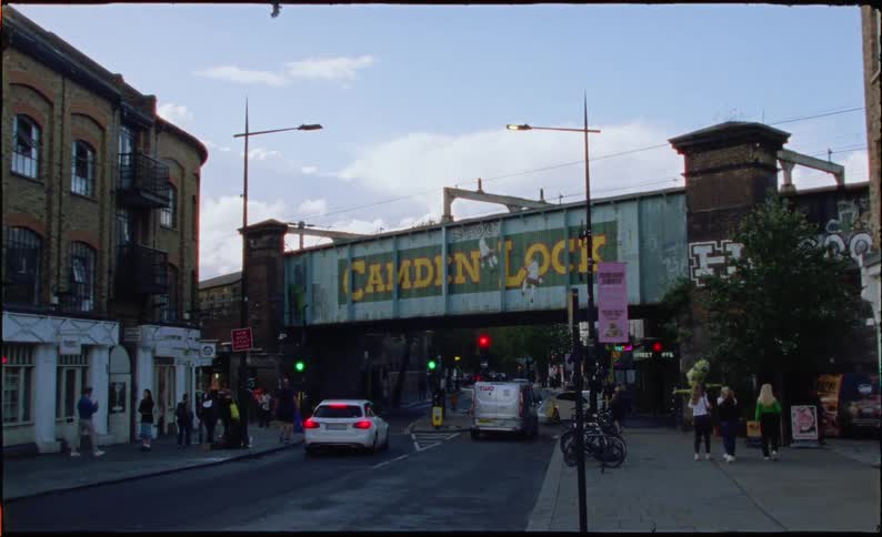 A shaky handheld shot reveals the iconic Camden Lock railway bridge over a bustling London street
