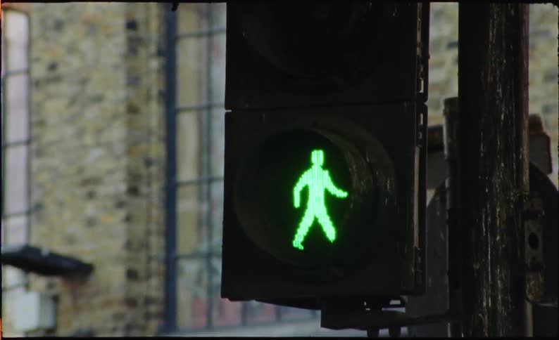 Chaotic and shaky handheld footage pans from a brick market hall building to a green pedestrian traffic light