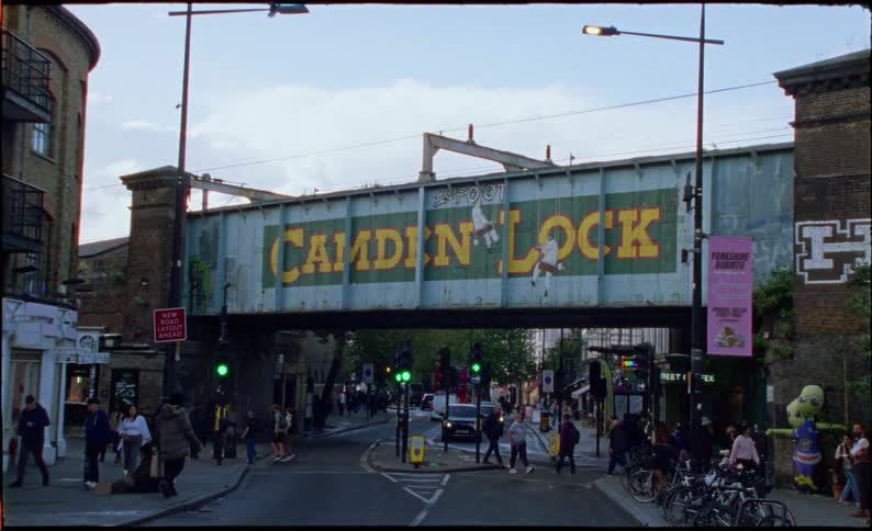 Vintage film-style view of the iconic Camden Lock railway bridge sign over a busy street in London