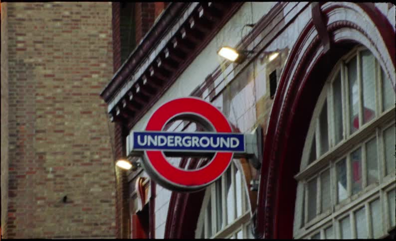 Vintage film footage captures a slow zoom-in on the iconic London Underground sign outside a classic station