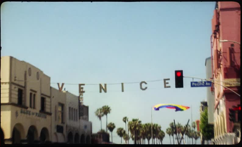 Vintage 8mm film captures the iconic Venice sign and a rainbow Pride flag waving on a sunny day with palm trees