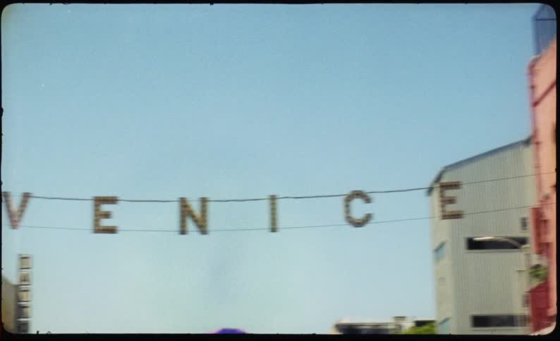 A handheld, vintage film-style pan across the iconic Venice sign on a sunny day in California