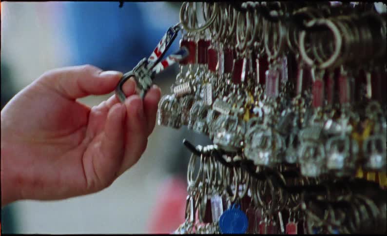 Close-up vintage film shot of a hand browsing shiny souvenir keychains at a tourist shop
