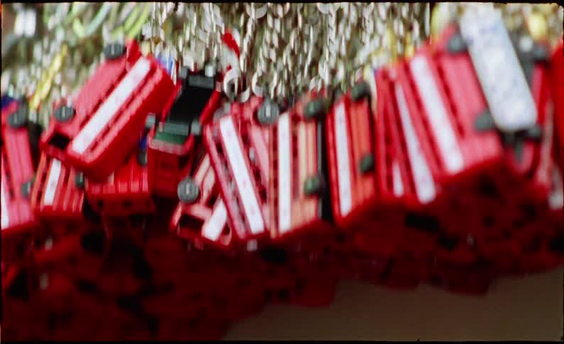 A close-up, handheld vintage film shot panning across a variety of classic London-themed souvenir keychains hanging in a shop
