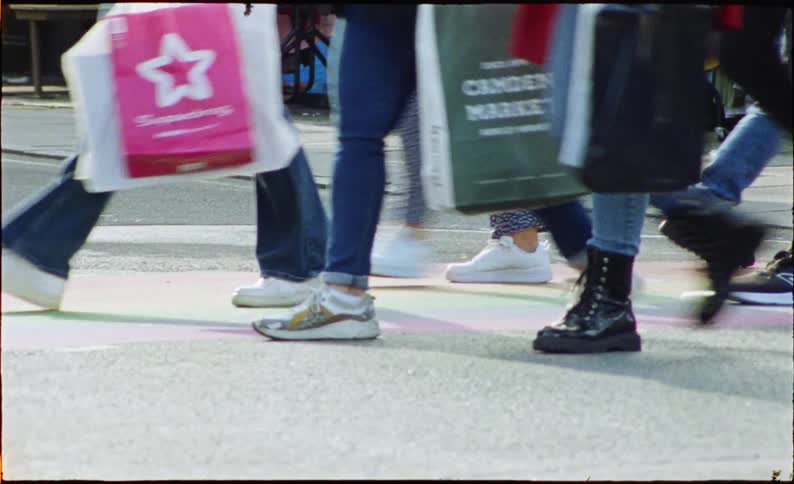 Low-angle, motion-blurred film footage of a crowd's legs and feet walking and cycling through a busy city street market