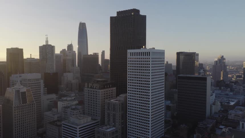 An aerial drone slowly pulls back over the dense cityscape of downtown San Francisco during a beautiful golden hour sunrise