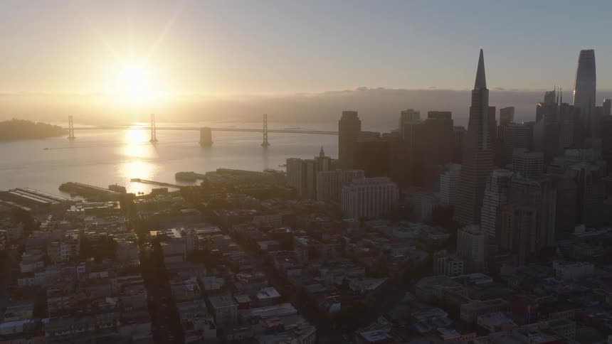 An epic aerial view of the San Francisco skyline and the Bay Bridge as the golden sun rises over the city