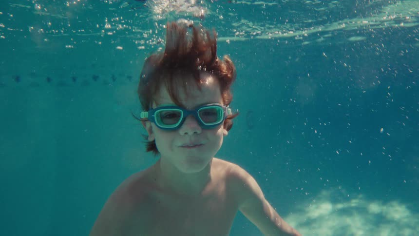 Young boy wearing swim goggles glides underwater in a clear blue swimming pool