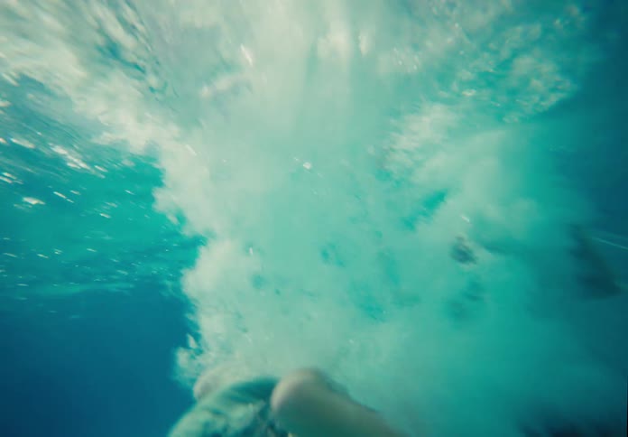 A young boy cannonballs into a backyard swimming pool in slow motion as the camera follows him underwater